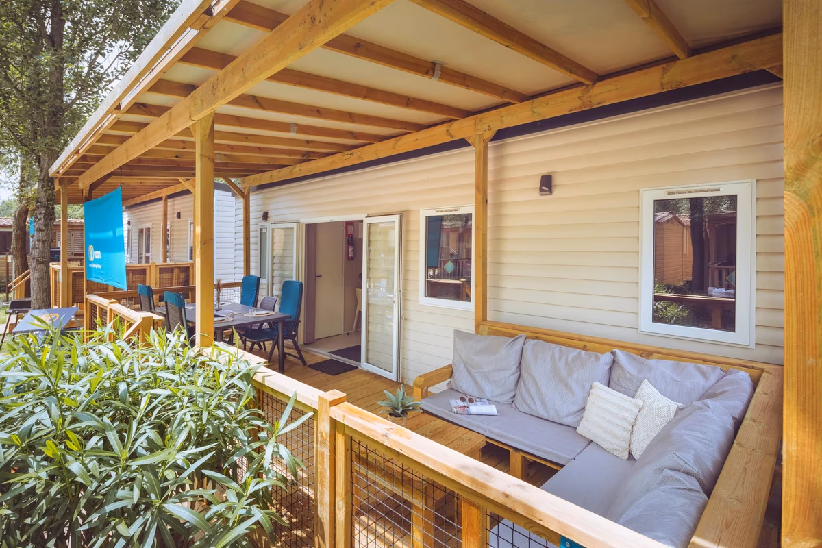 Overdekte veranda met een hoekbank en een eettafel met blauwe stoelen bij een stacaravan