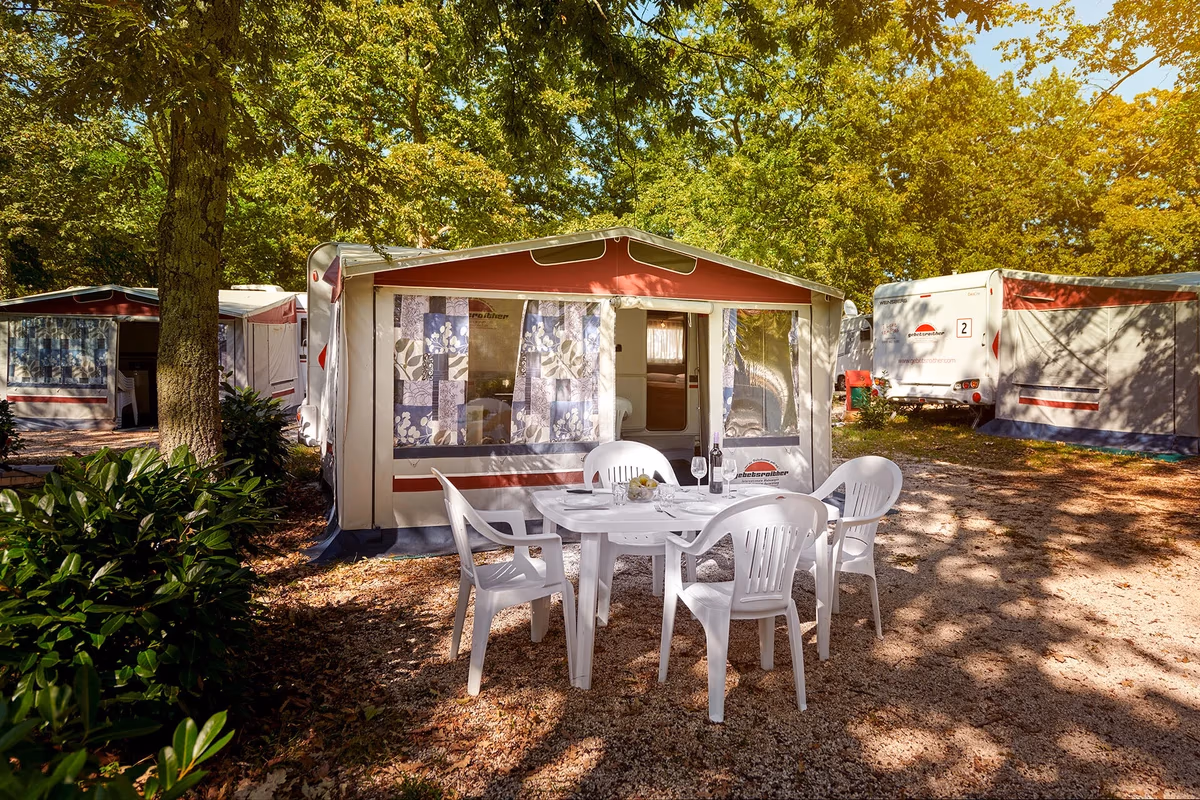 Tourcaravan met voortent op Camping Bijela Uvala, met witte tuinstoelen rond een gedekte tafel op het grind