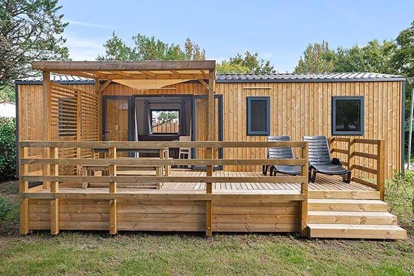 Stacaravan met houten gevel en een ruim vlonderterras met twee ligbedden en een pergola op Camping Bijela Uvala