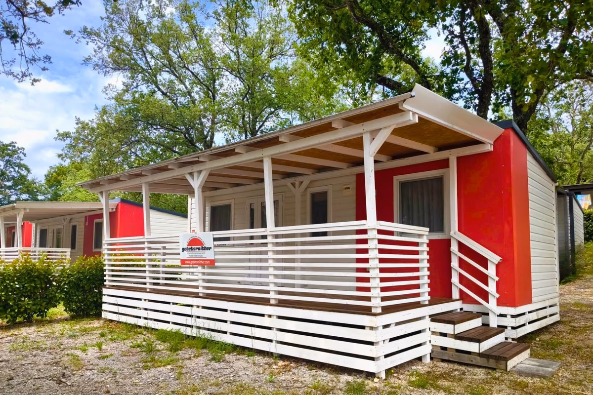 Rood-witte stacaravan met een wit overdekt terras en een witte reling op Camping Bijela Uvala