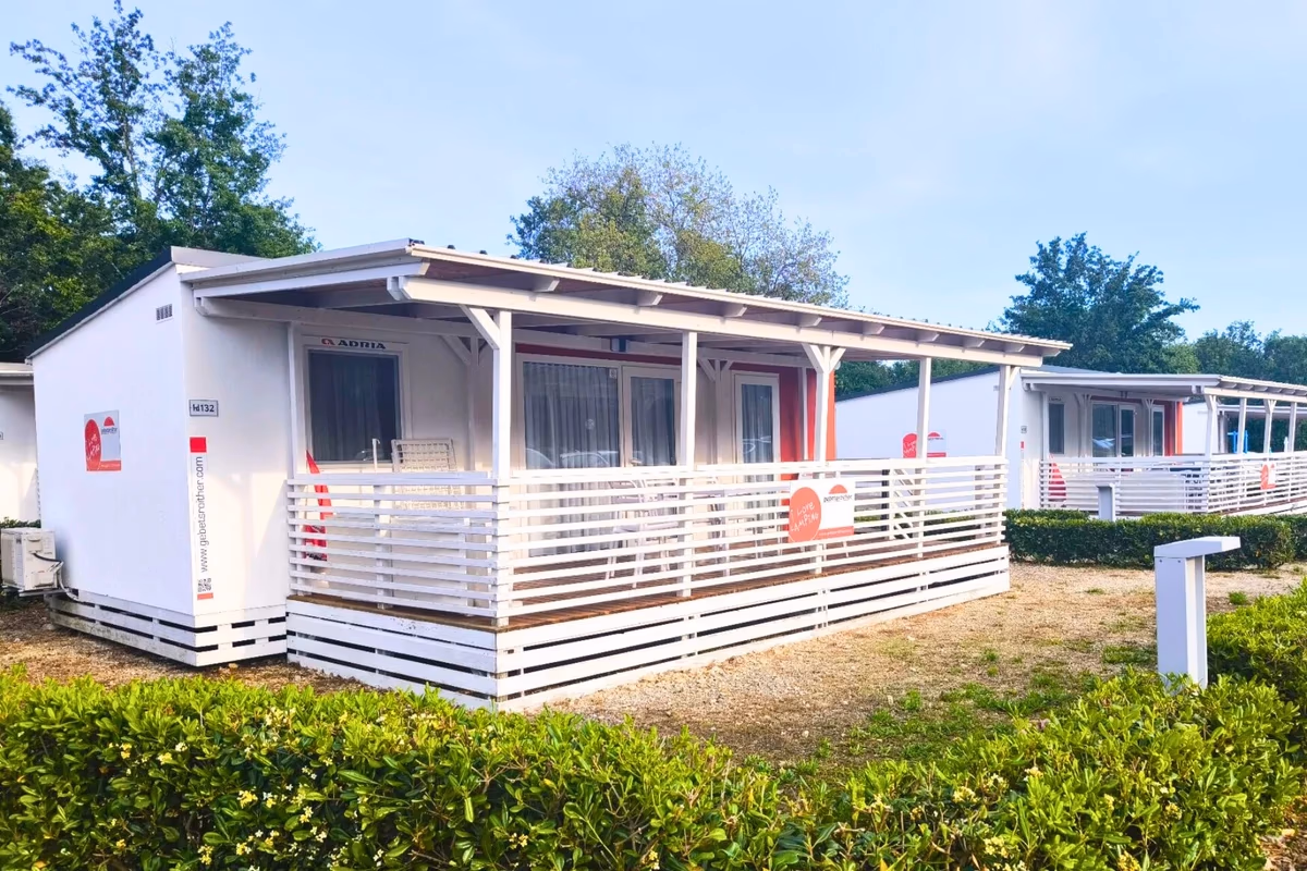 Witte stacaravan met rode accenten en een witte terrasafscheiding op Camping Bijela Uvala, met een rij vergelijkbare huisjes erachter