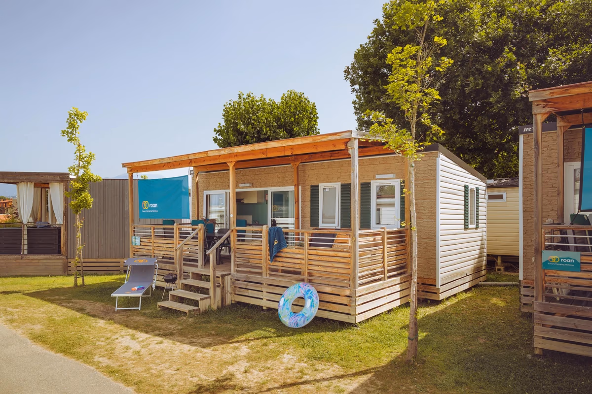 Stacaravan met houten overkapping en veranda op Camping Bijela Uvala, met een ligbed en een zwemband in het gras