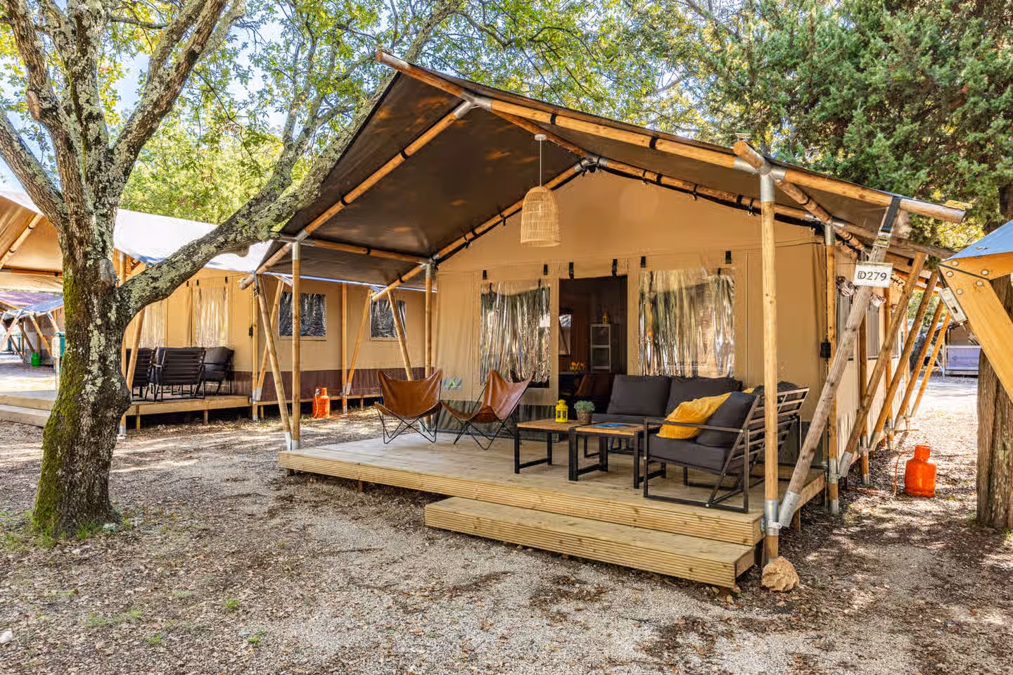 Safaritent met vlinderstoelen en een loungeset op het houten terras, onder de bomen op Camping Bijela Uvala