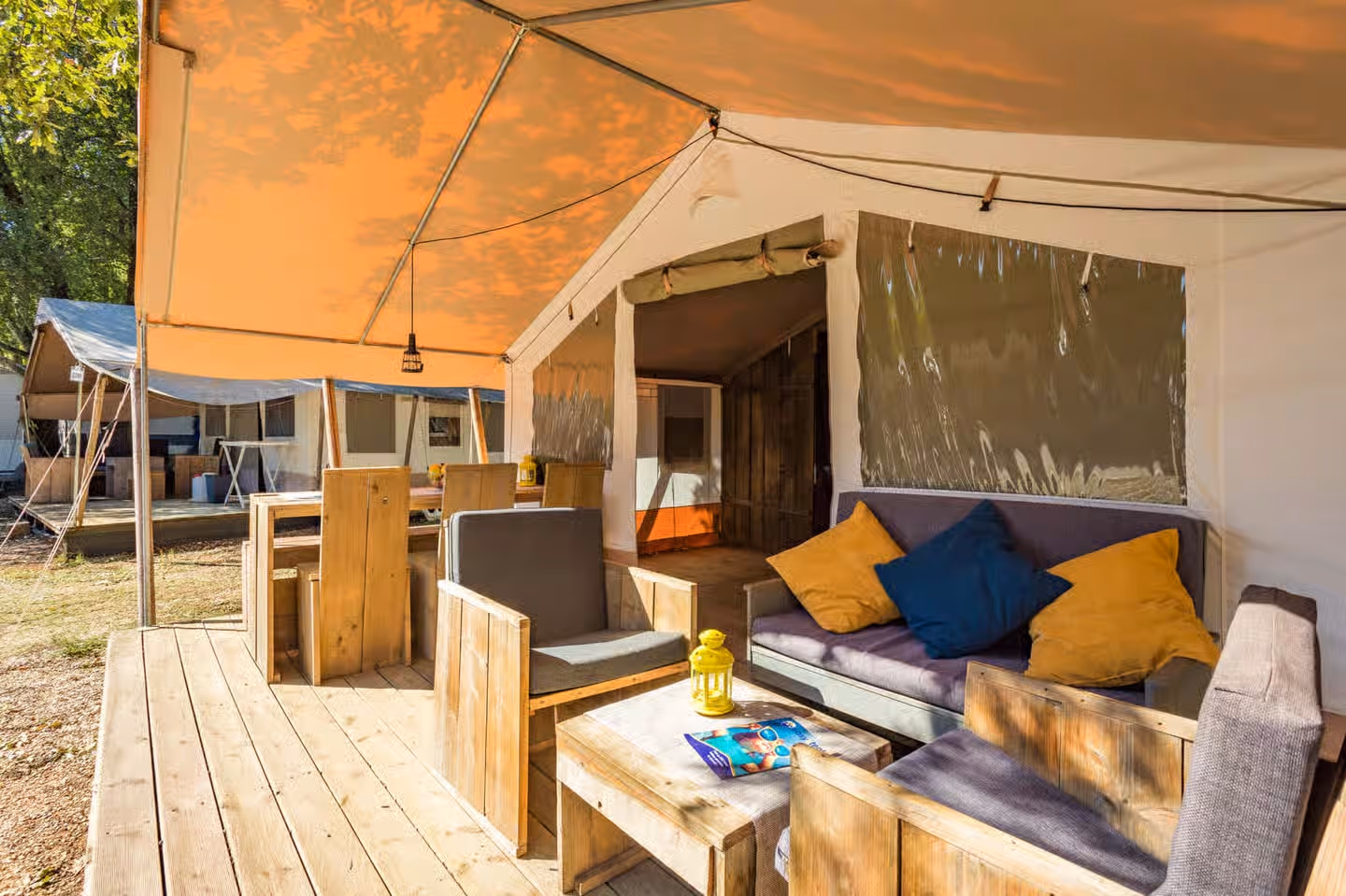 Terras onder de luifel van een safaritent op Camping Bijela Uvala, met een loungebank met gekleurde kussens en een houten salontafel
