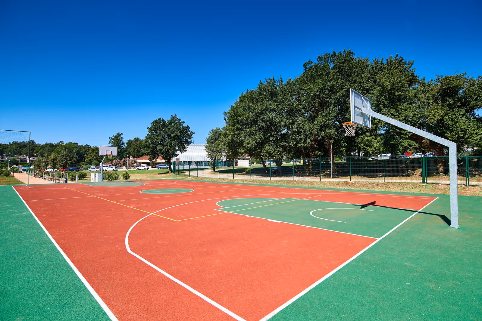 Rood-groen basketbalveld met doelen en bomen eromheen op Camping Bijela Uvala