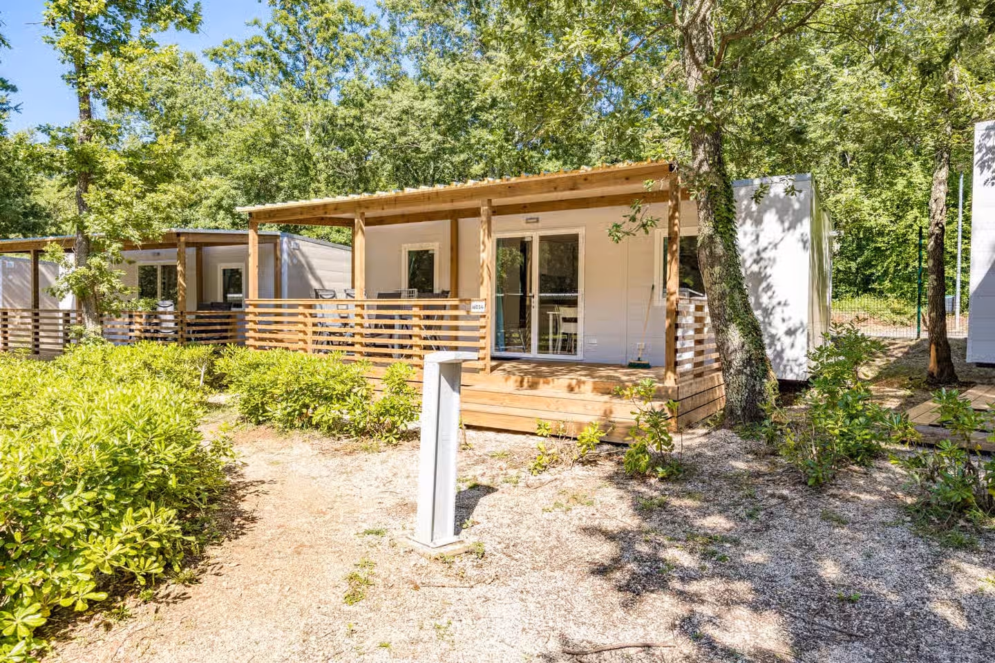 Stacaravan met een houten terras op een beboste plek met grind en struiken op Camping Bijela Uvala