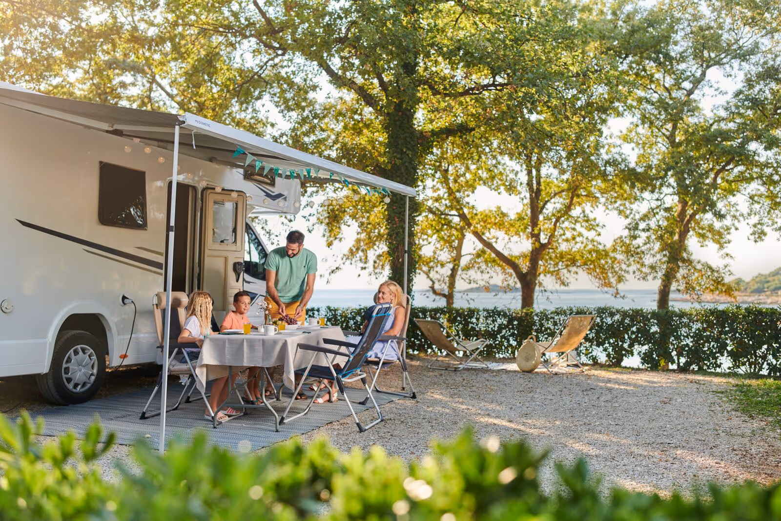 Gezin aan tafel naast een camper op een schaduwrijke plaats aan zee, Camping Bijela Uvala