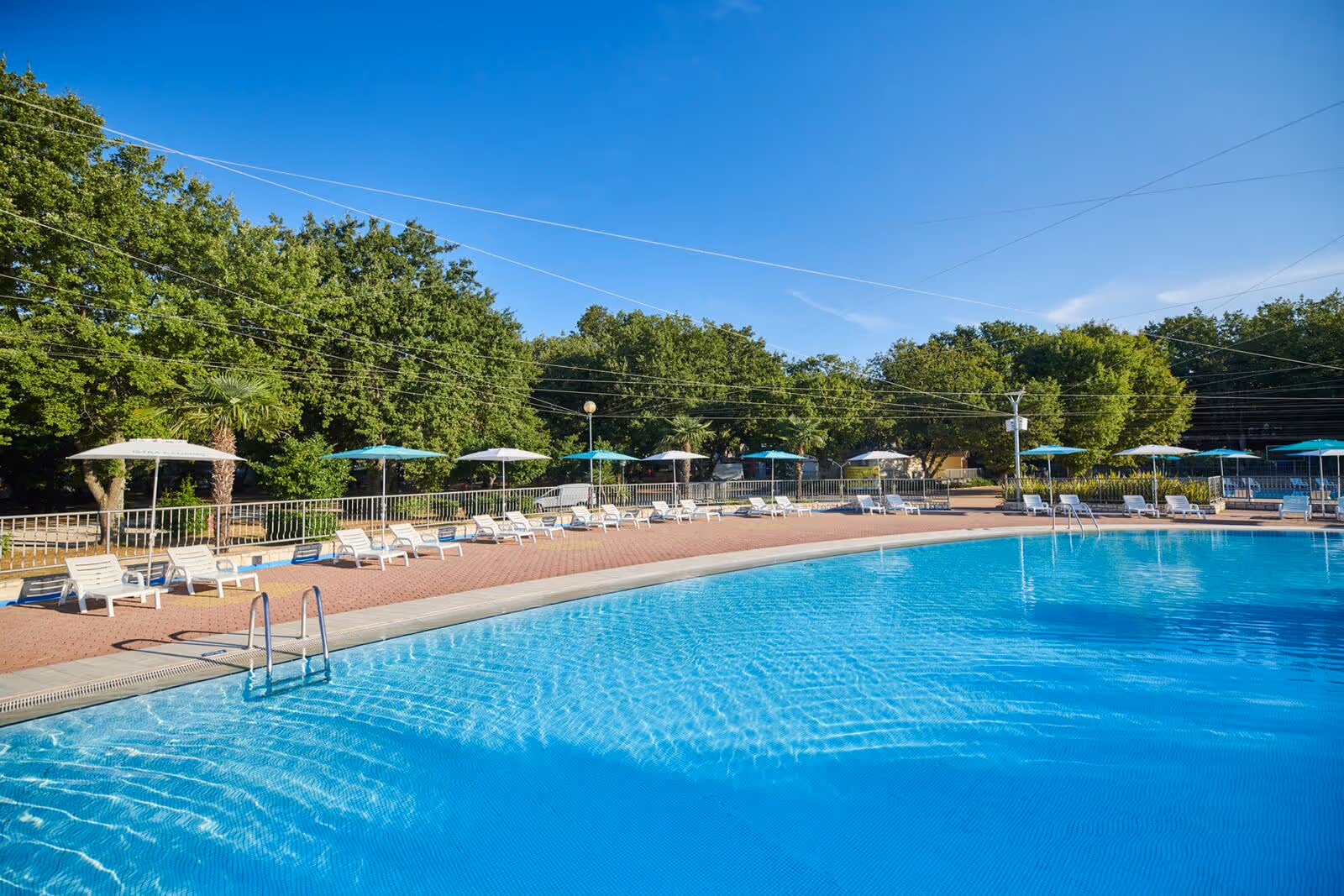 Groot buitenzwembad met ligbedden, parasols en bomen op de achtergrond, Camping Bijela Uvala