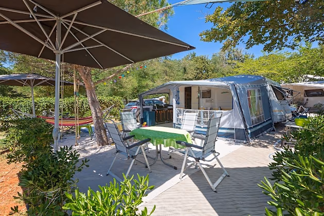 Luxury staanplaats van Camping Bijela Uvala met caravan, parasol, hangmat en groen terras