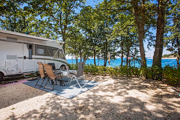 Luxury Mare staanplaats met camper en zitje onder de bomen, met uitzicht op zee
