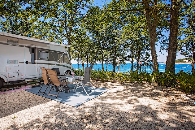 Luxury Mare staanplaats met camper en zitje onder de bomen, met uitzicht op zee