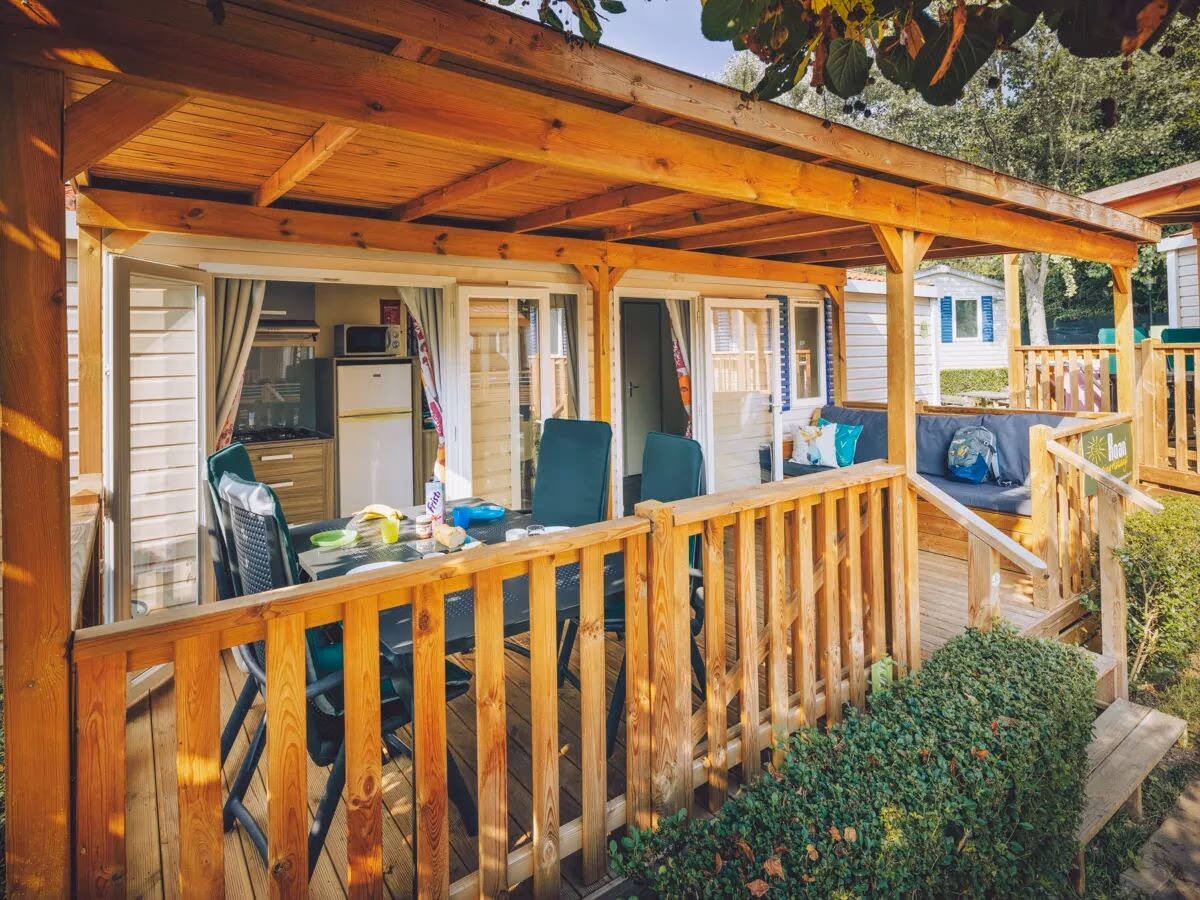 Veranda met een eettafel en stoelen bij een stacaravan, met doorkijk naar de keuken met koelkast en magnetron