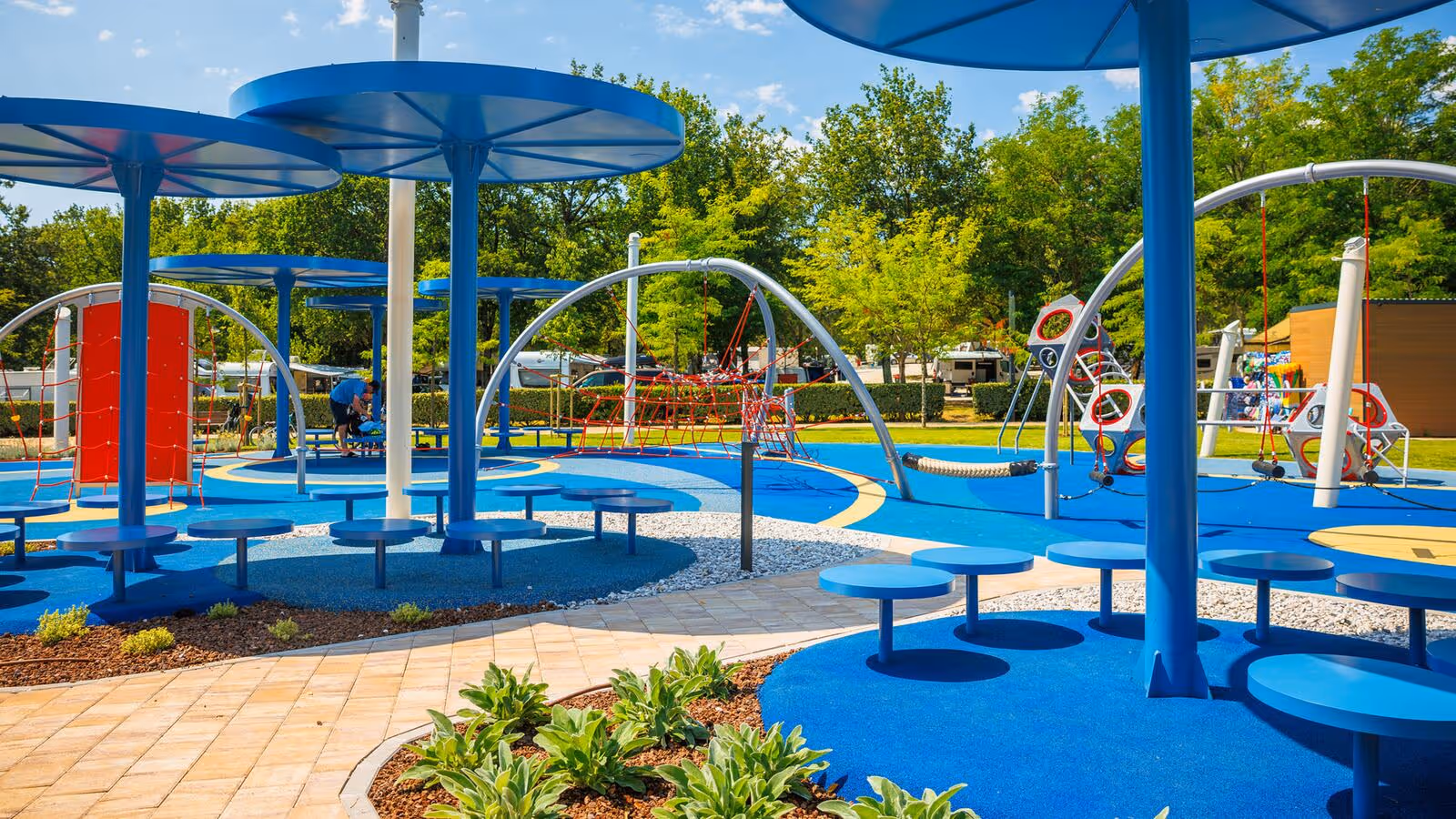 Kleurrijke speelzone met ronde schaduwdoeken, tafels en speeltoestellen op Camping Bijela Uvala