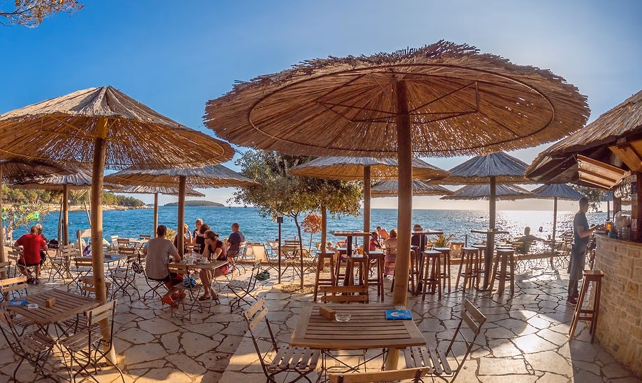 Strandbar met rieten parasols, houten tafels en barkrukken aan zee op Camping Bijela Uvala