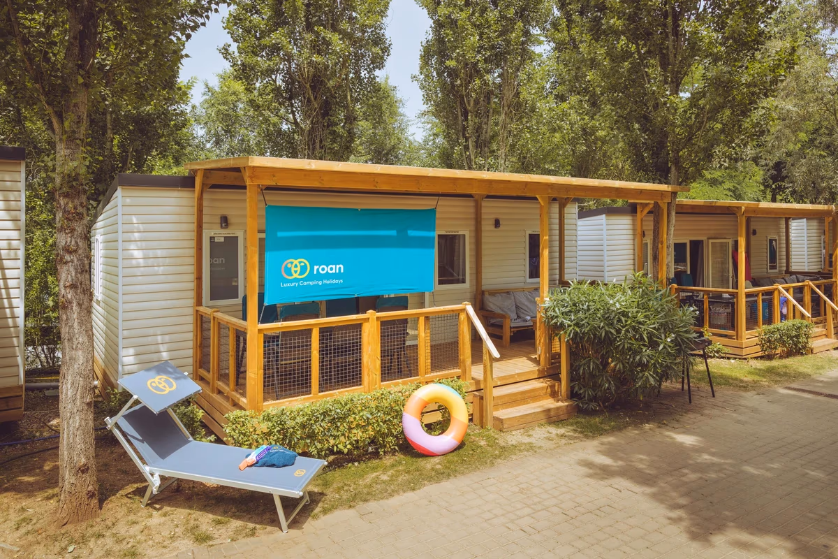 Stacaravan met een brede overkapping en een doek als zonwering, met een ligbed op het pad ervoor