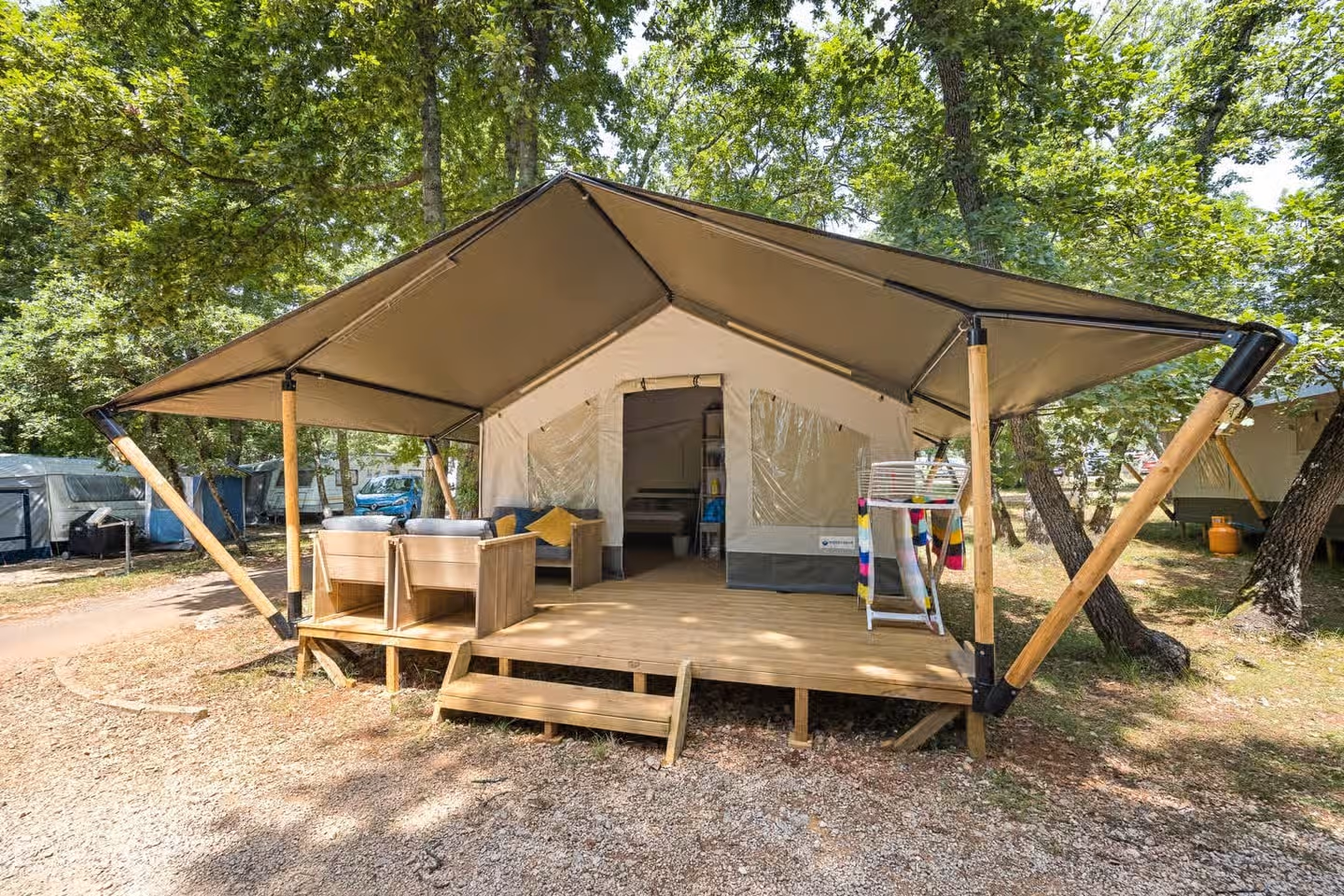 Safaritent met een brede luifel op houten schoren en loungebankjes op het terras, tussen de eiken