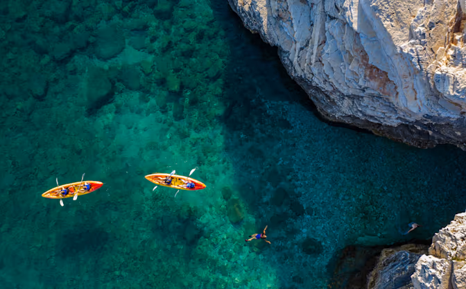 Twee kajaks en een zwemmer in helder turquoise water langs de rotskust bij Camping Bijela Uvala